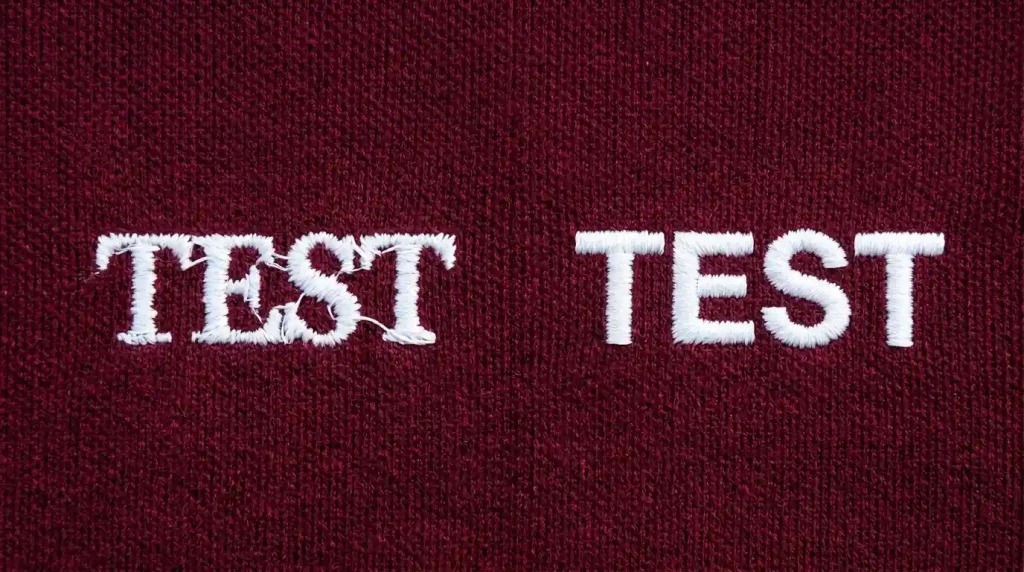 Side by side comparison of thin decorative font versus bold sans-serif font for small embroidery text on burgundy polo